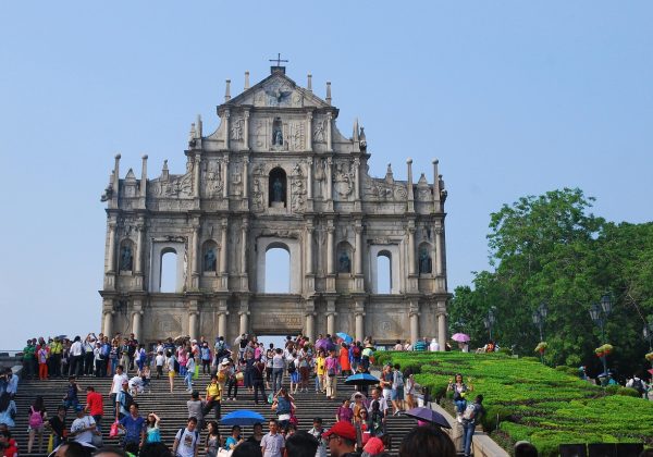 澳门大三巴牌坊在金色晨光下的宏伟全景，游客络绎不绝，葡式巴洛克石雕细节清晰可见，是澳门之旅最具标志性的打卡胜地